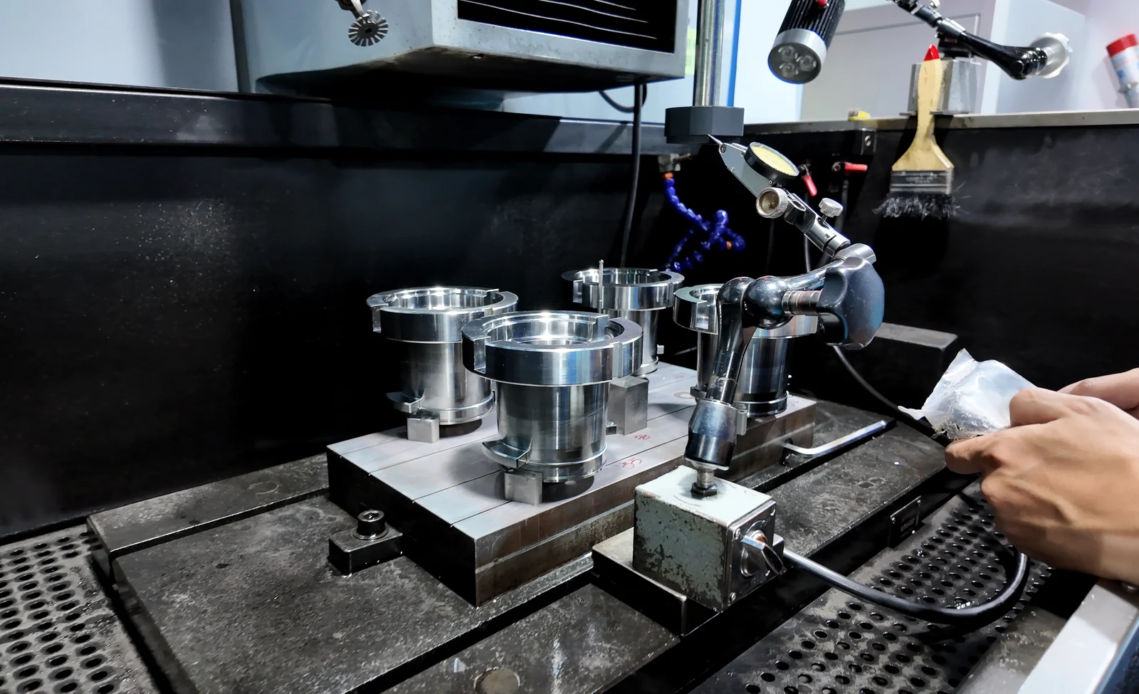Mold components set up inside machining equipment with a dial indicator and operator hands
