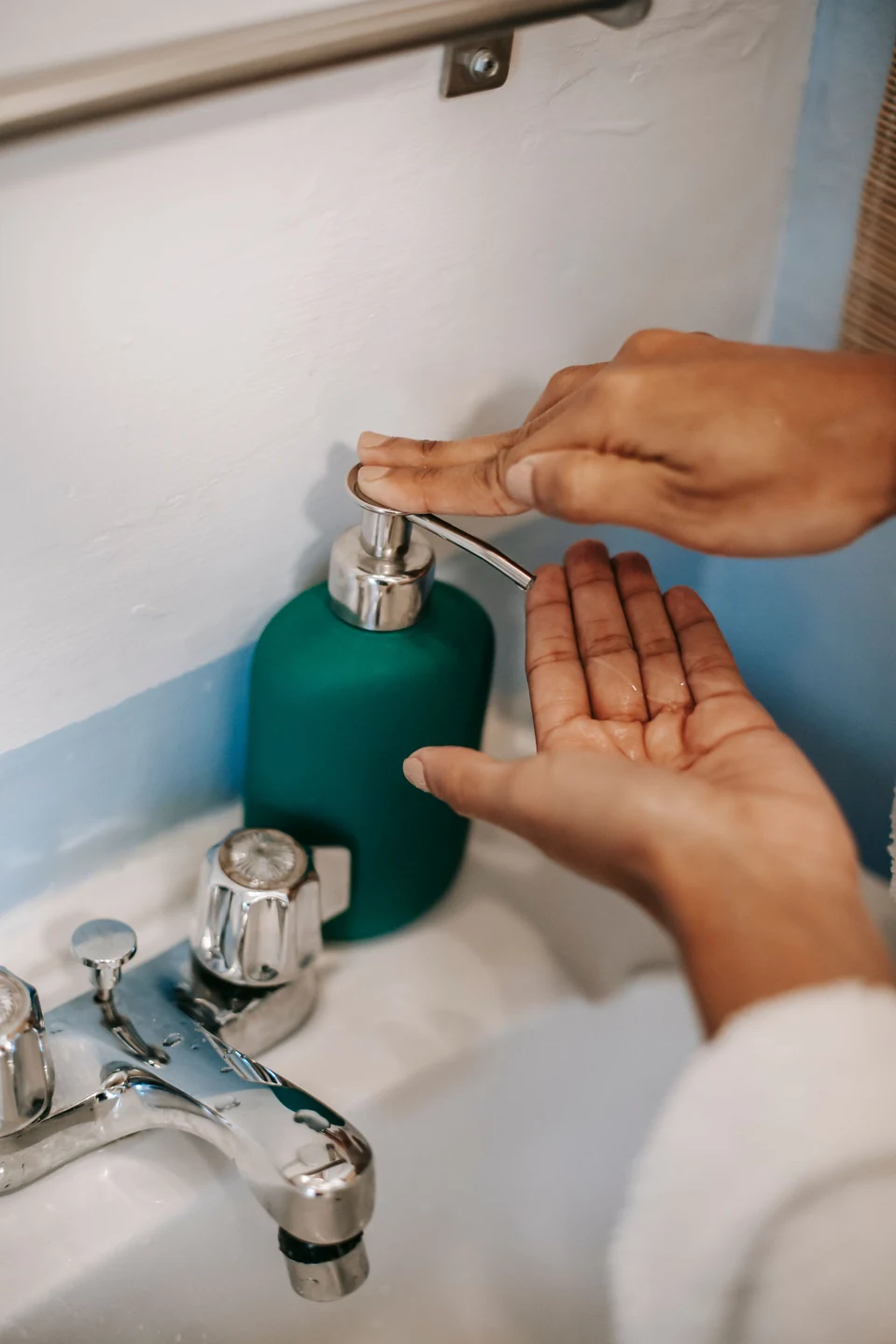 Hands using a pump soap dispenser beside a bathroom sink